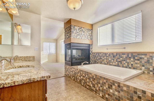 bathroom featuring vaulted ceiling, vanity, a relaxing tiled tub, and a wealth of natural light