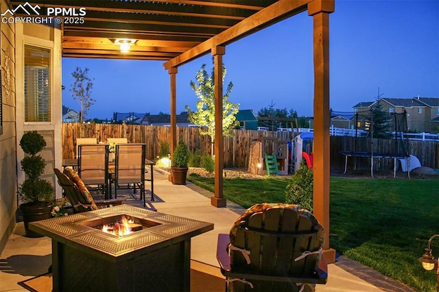 patio terrace at dusk with an outdoor fire pit, a yard, a trampoline, and a pergola