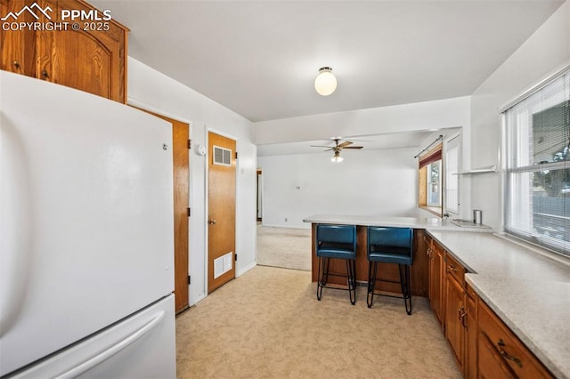 kitchen featuring ceiling fan, white fridge, kitchen peninsula, a kitchen breakfast bar, and light carpet