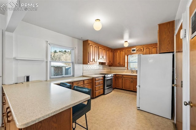 kitchen with electric stove, tasteful backsplash, white fridge, kitchen peninsula, and a kitchen bar