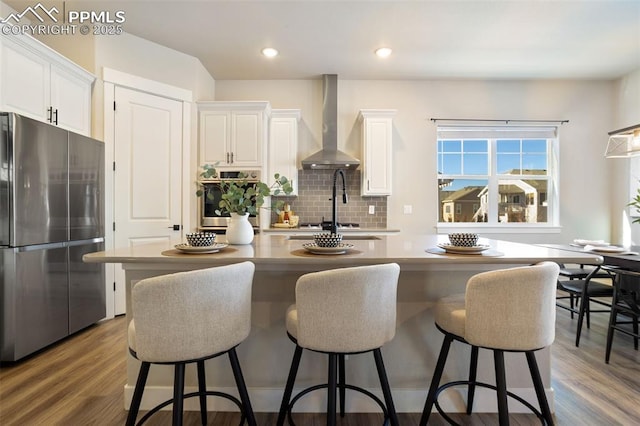 kitchen featuring backsplash, white cabinets, wall chimney range hood, and appliances with stainless steel finishes