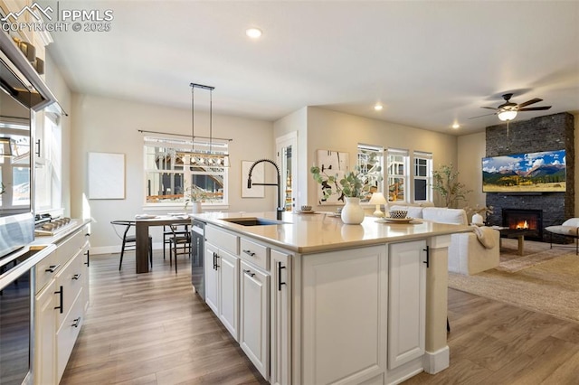 kitchen with sink, hanging light fixtures, stainless steel oven, a kitchen island with sink, and white cabinets