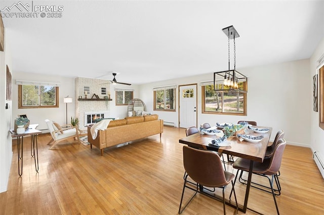 dining room featuring a brick fireplace, ceiling fan with notable chandelier, light hardwood / wood-style floors, and a baseboard heating unit