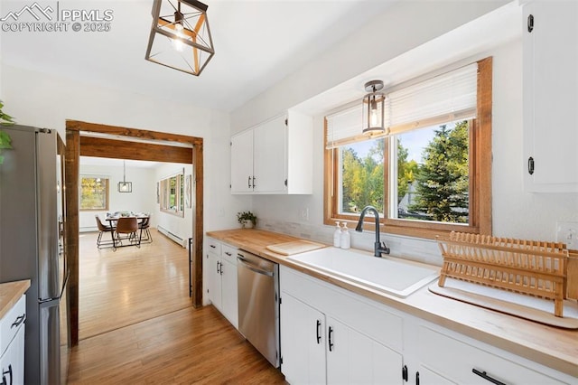 kitchen with sink, hanging light fixtures, a baseboard heating unit, stainless steel appliances, and white cabinets