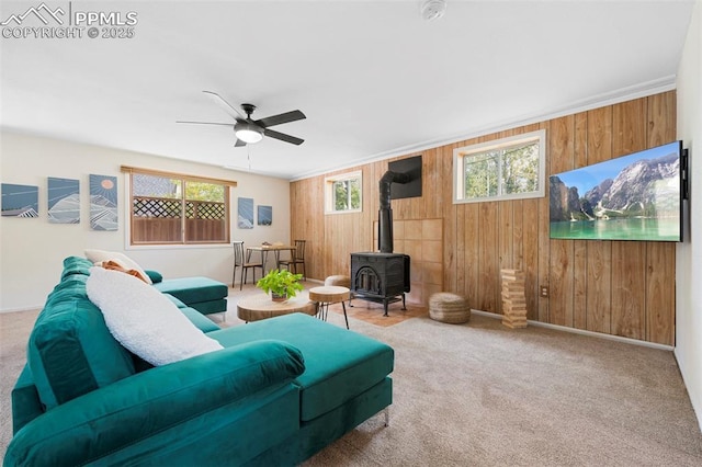 carpeted living room featuring wooden walls, ceiling fan, and a wood stove