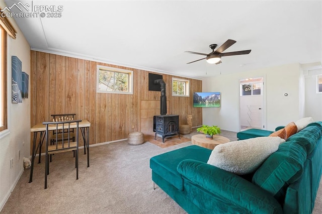 carpeted living room featuring wooden walls, ceiling fan, and a wood stove