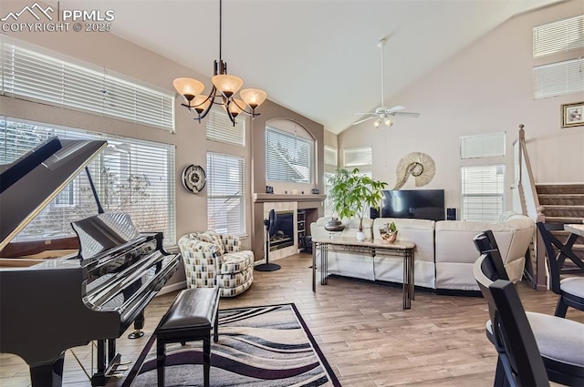 living room with ceiling fan with notable chandelier, high vaulted ceiling, light hardwood / wood-style flooring, and a tiled fireplace