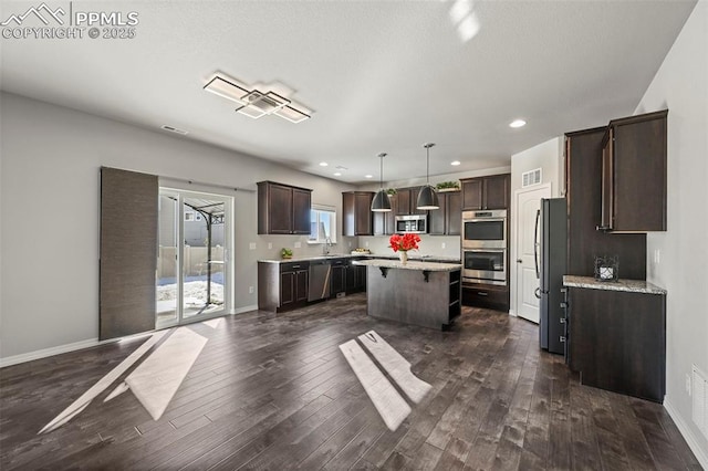 kitchen featuring dark brown cabinets, a kitchen island, decorative light fixtures, and appliances with stainless steel finishes