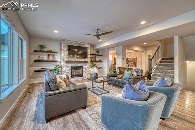 living room featuring hardwood / wood-style flooring, a stone fireplace, and ceiling fan