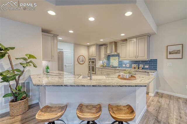 kitchen featuring kitchen peninsula, appliances with stainless steel finishes, a kitchen bar, light wood-type flooring, and wall chimney exhaust hood