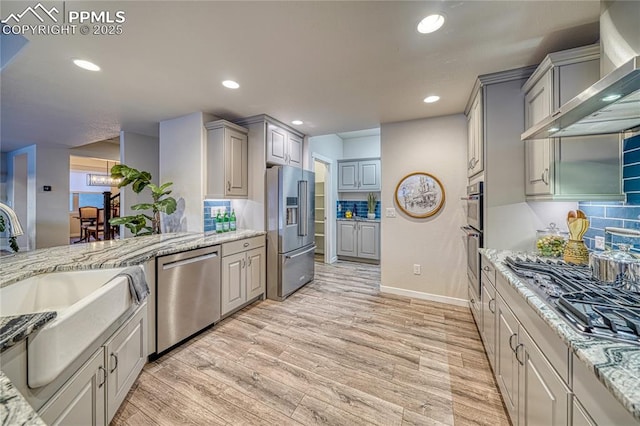 kitchen with light stone countertops, appliances with stainless steel finishes, wall chimney exhaust hood, and gray cabinetry