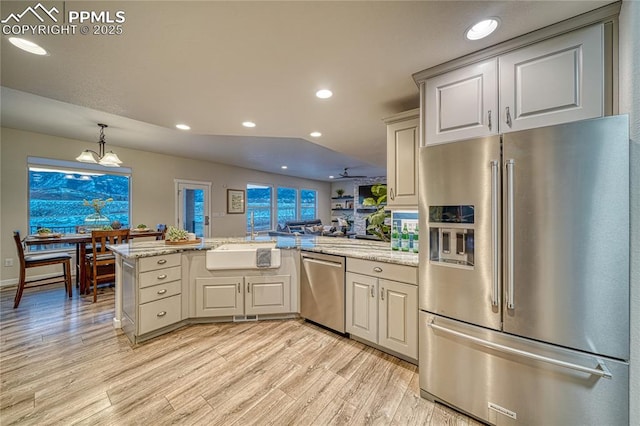 kitchen with kitchen peninsula, appliances with stainless steel finishes, light stone counters, sink, and light hardwood / wood-style floors