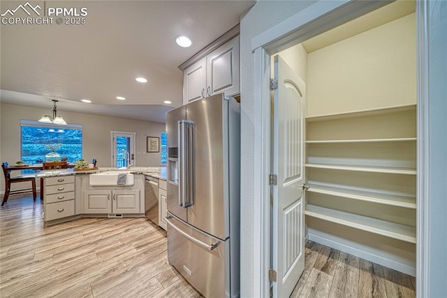 kitchen featuring sink, light wood-type flooring, a notable chandelier, kitchen peninsula, and stainless steel appliances