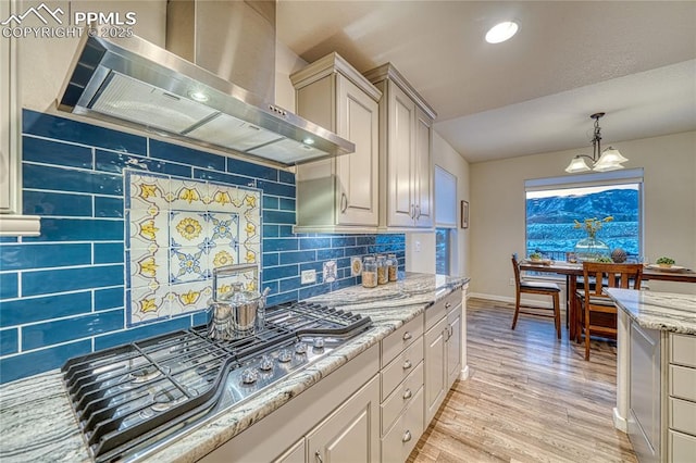 kitchen with hanging light fixtures, wall chimney exhaust hood, decorative backsplash, light wood-type flooring, and stainless steel gas cooktop