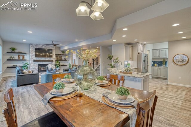 dining area with a stone fireplace, light hardwood / wood-style floors, and ceiling fan with notable chandelier