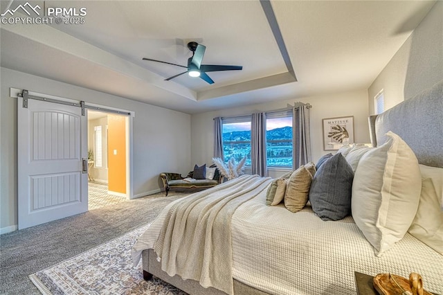 carpeted bedroom with ceiling fan, a barn door, and a raised ceiling