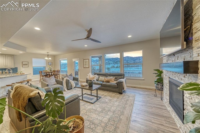 living room featuring a fireplace, ceiling fan with notable chandelier, a wealth of natural light, and sink