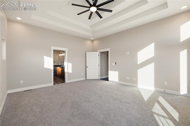 unfurnished bedroom featuring a high ceiling, a raised ceiling, ensuite bathroom, and carpet