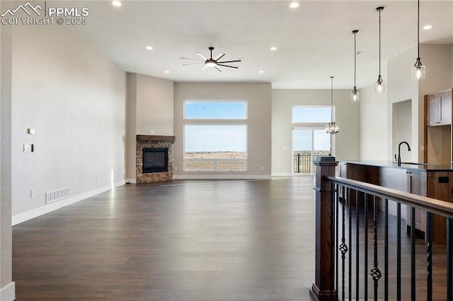 living room with ceiling fan with notable chandelier, dark wood-type flooring, sink, and a stone fireplace