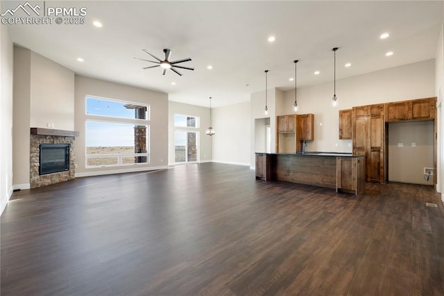 kitchen with ceiling fan, hanging light fixtures, a stone fireplace, and dark wood-type flooring