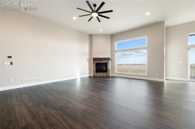 unfurnished living room with ceiling fan, dark hardwood / wood-style floors, and a stone fireplace