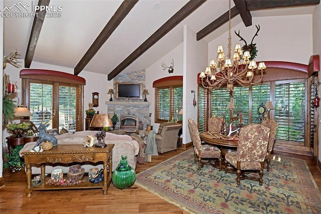 dining area featuring wood-type flooring, high vaulted ceiling, an inviting chandelier, and a stone fireplace