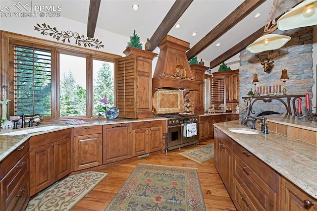 kitchen featuring light wood-type flooring, premium range hood, double oven range, and sink