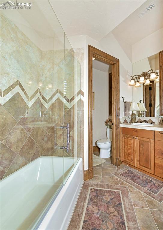 full bathroom with combined bath / shower with glass door, vanity, and toilet