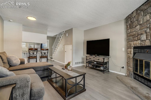 living room featuring a stone fireplace, wood-type flooring, and a textured ceiling