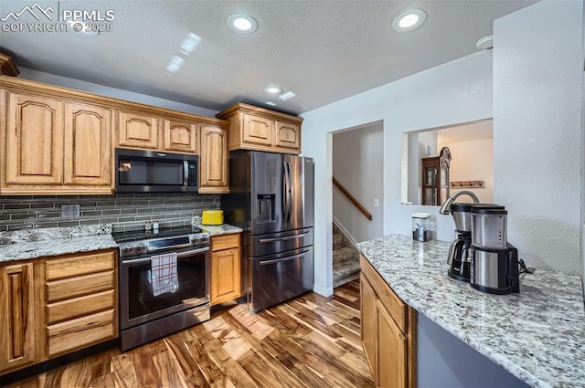 kitchen with stainless steel appliances, light stone countertops, light hardwood / wood-style floors, and decorative backsplash