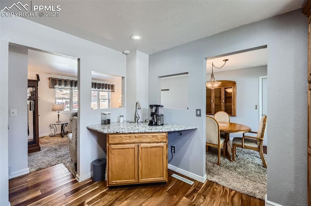 kitchen featuring light stone counters, hanging light fixtures, dark hardwood / wood-style floors, and a textured ceiling