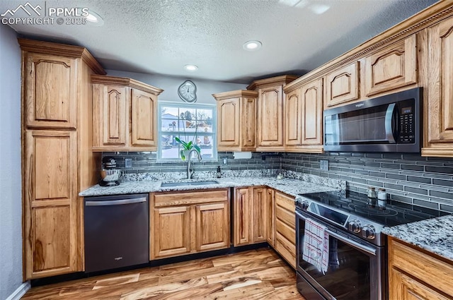 kitchen featuring sink, light hardwood / wood-style flooring, stainless steel appliances, tasteful backsplash, and light stone countertops