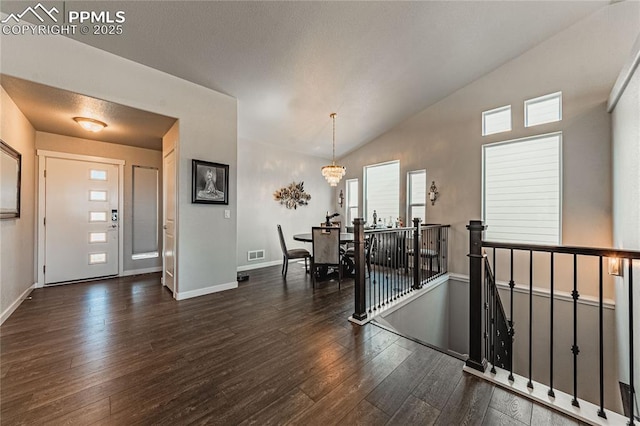 foyer with dark hardwood / wood-style floors, lofted ceiling, and a notable chandelier