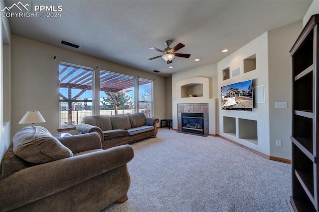 carpeted living room with a tiled fireplace, ceiling fan, and a textured ceiling