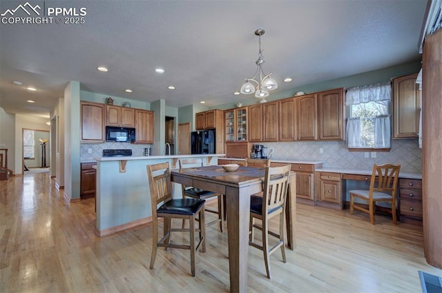 kitchen featuring light wood-type flooring, decorative light fixtures, a kitchen island, and black appliances