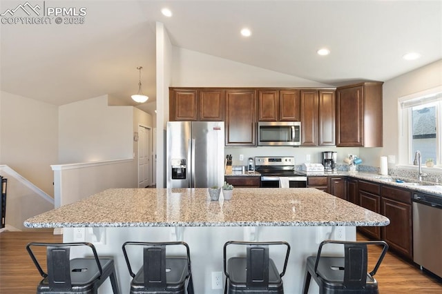 kitchen featuring hanging light fixtures, sink, vaulted ceiling, appliances with stainless steel finishes, and a kitchen island