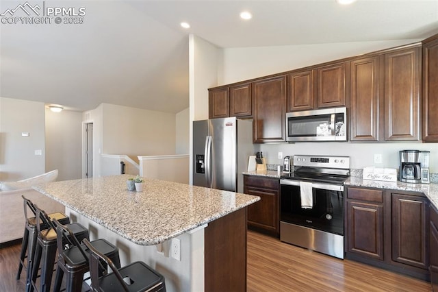 kitchen featuring a kitchen island, stainless steel appliances, a breakfast bar area, and vaulted ceiling