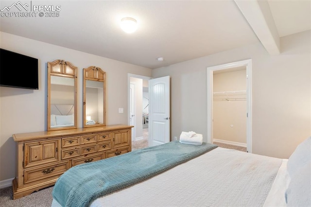 bedroom featuring beam ceiling, a walk in closet, light carpet, and a closet