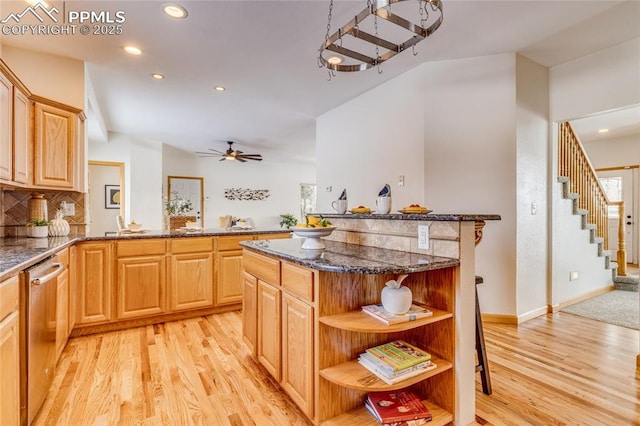 kitchen with ceiling fan, backsplash, dark stone counters, stainless steel dishwasher, and light hardwood / wood-style flooring