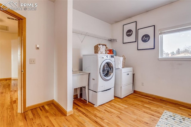 clothes washing area with separate washer and dryer and light hardwood / wood-style floors