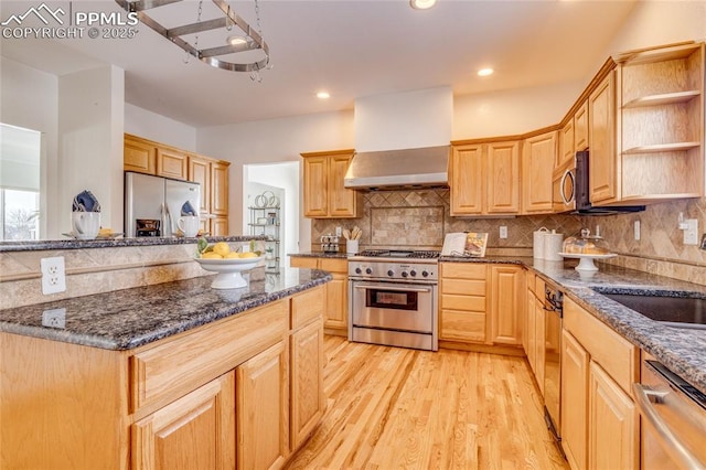 kitchen featuring wall chimney range hood, stainless steel appliances, tasteful backsplash, light brown cabinetry, and light hardwood / wood-style floors