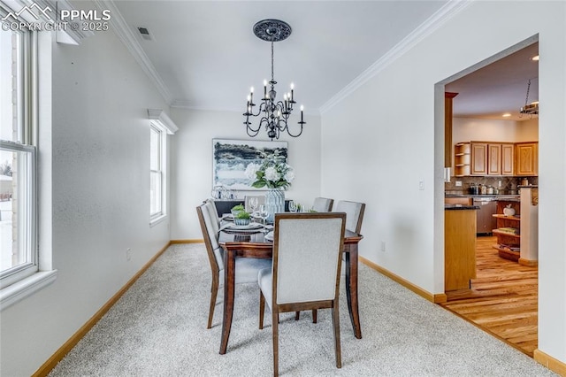 dining area featuring crown molding, a chandelier, a healthy amount of sunlight, and light colored carpet