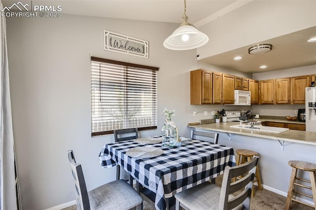 kitchen featuring white appliances, hanging light fixtures, sink, a breakfast bar, and vaulted ceiling