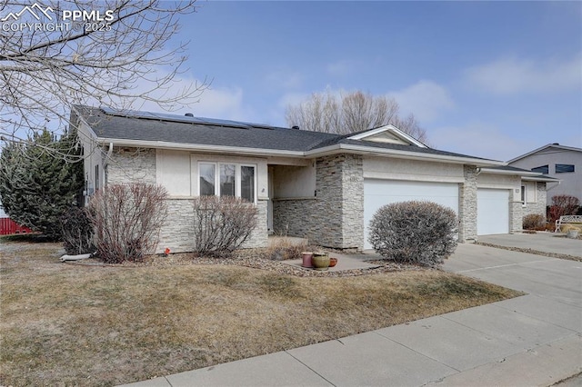 single story home featuring solar panels, concrete driveway, an attached garage, stone siding, and a front lawn