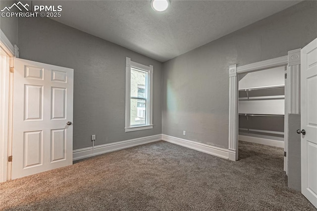 unfurnished bedroom featuring a spacious closet, a closet, dark carpet, and a textured ceiling