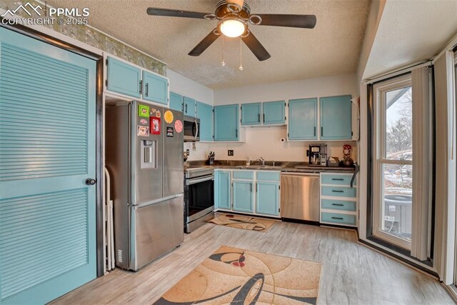 kitchen with appliances with stainless steel finishes, ceiling fan, blue cabinets, and a textured ceiling