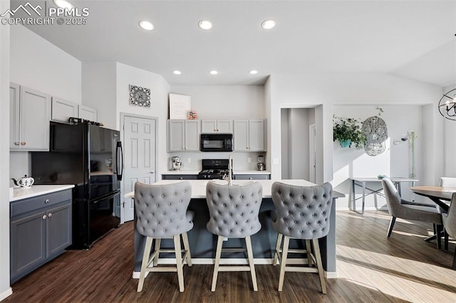 kitchen with dark hardwood / wood-style floors, black appliances, a kitchen island with sink, and gray cabinetry