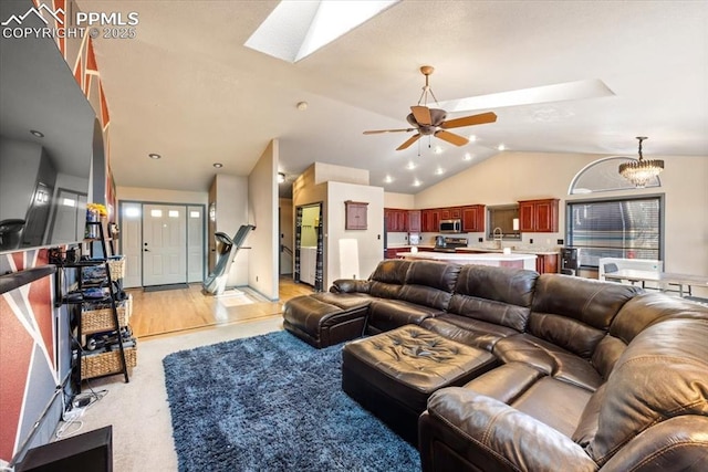 living room with lofted ceiling with skylight, sink, and ceiling fan with notable chandelier