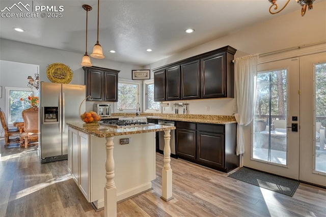 kitchen with appliances with stainless steel finishes, pendant lighting, light hardwood / wood-style flooring, a kitchen island, and plenty of natural light