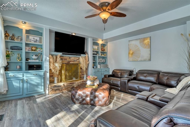 living room featuring built in shelves, ceiling fan, a fireplace, and light hardwood / wood-style floors